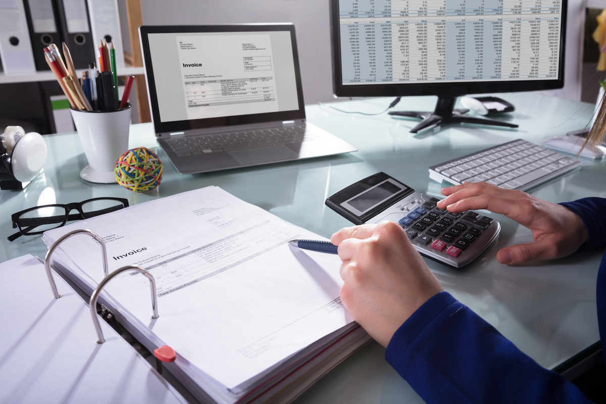 Close-up Of A Businessperson's Hand Calculating Invoice At Workplace Woman using calculator